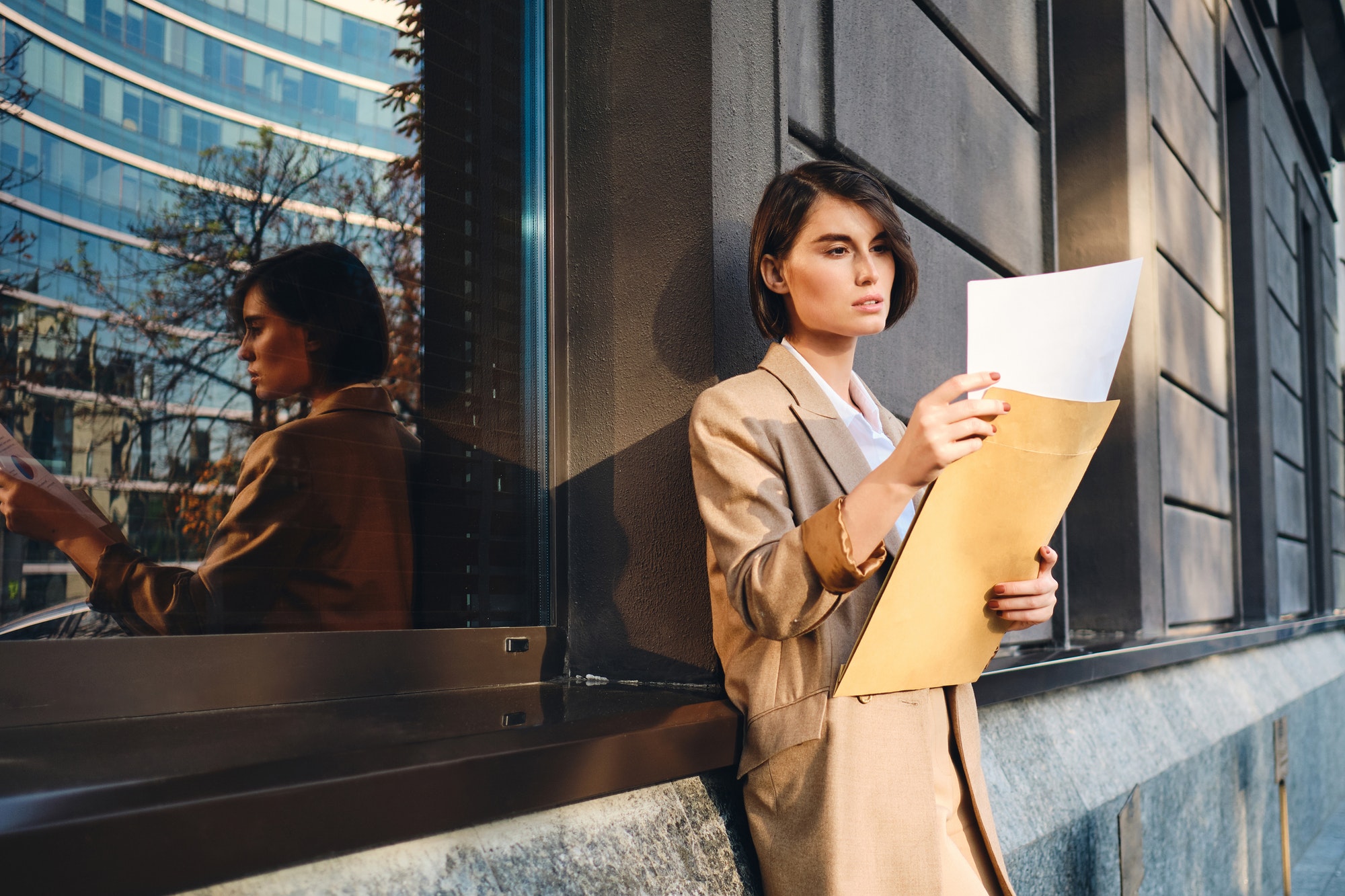 Young confident stylish businesswoman thoughtfully working with papers outdoor