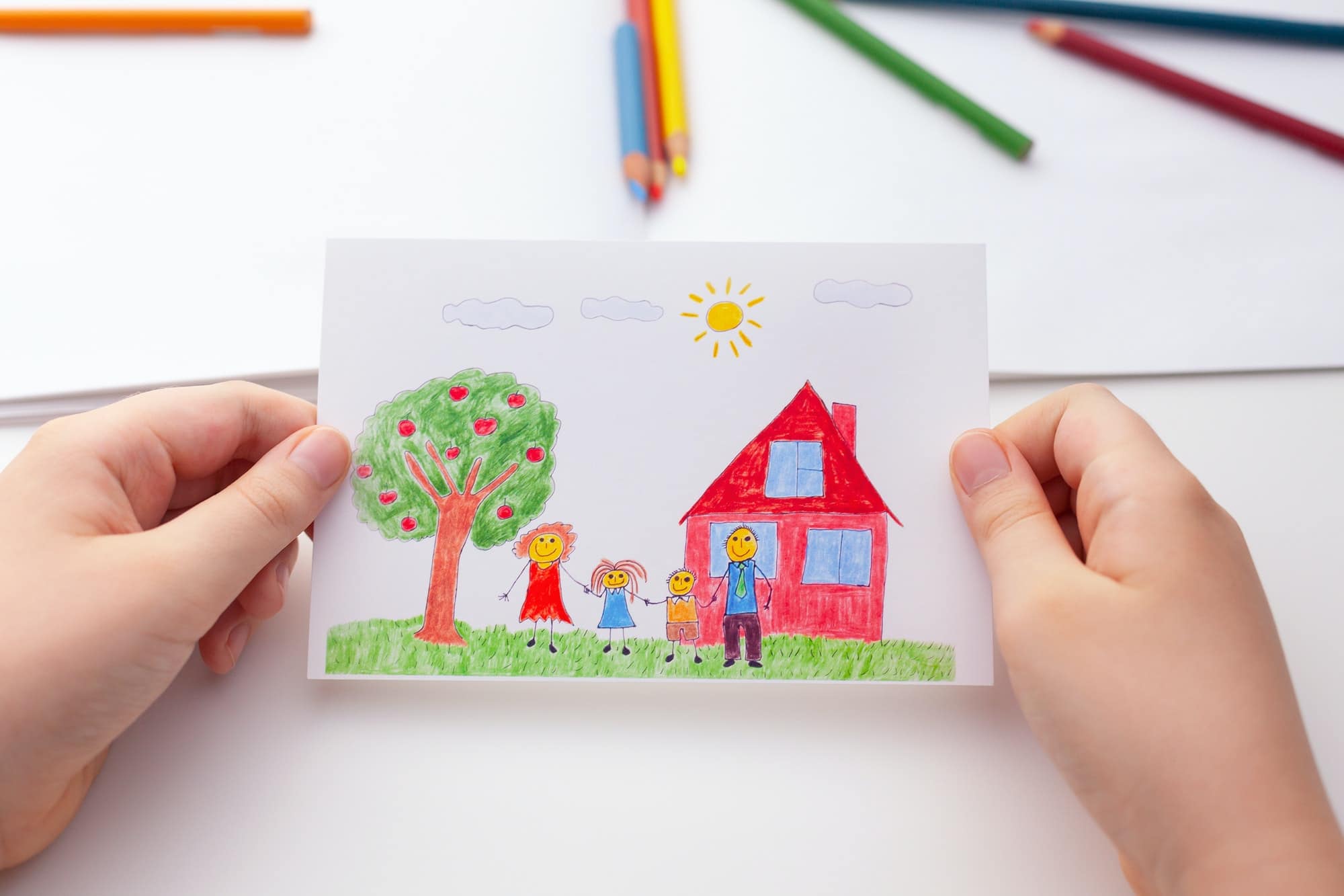 孩子拿着一幅画，上面有一个幸福的家庭、一棵苹果树和一栋房子
