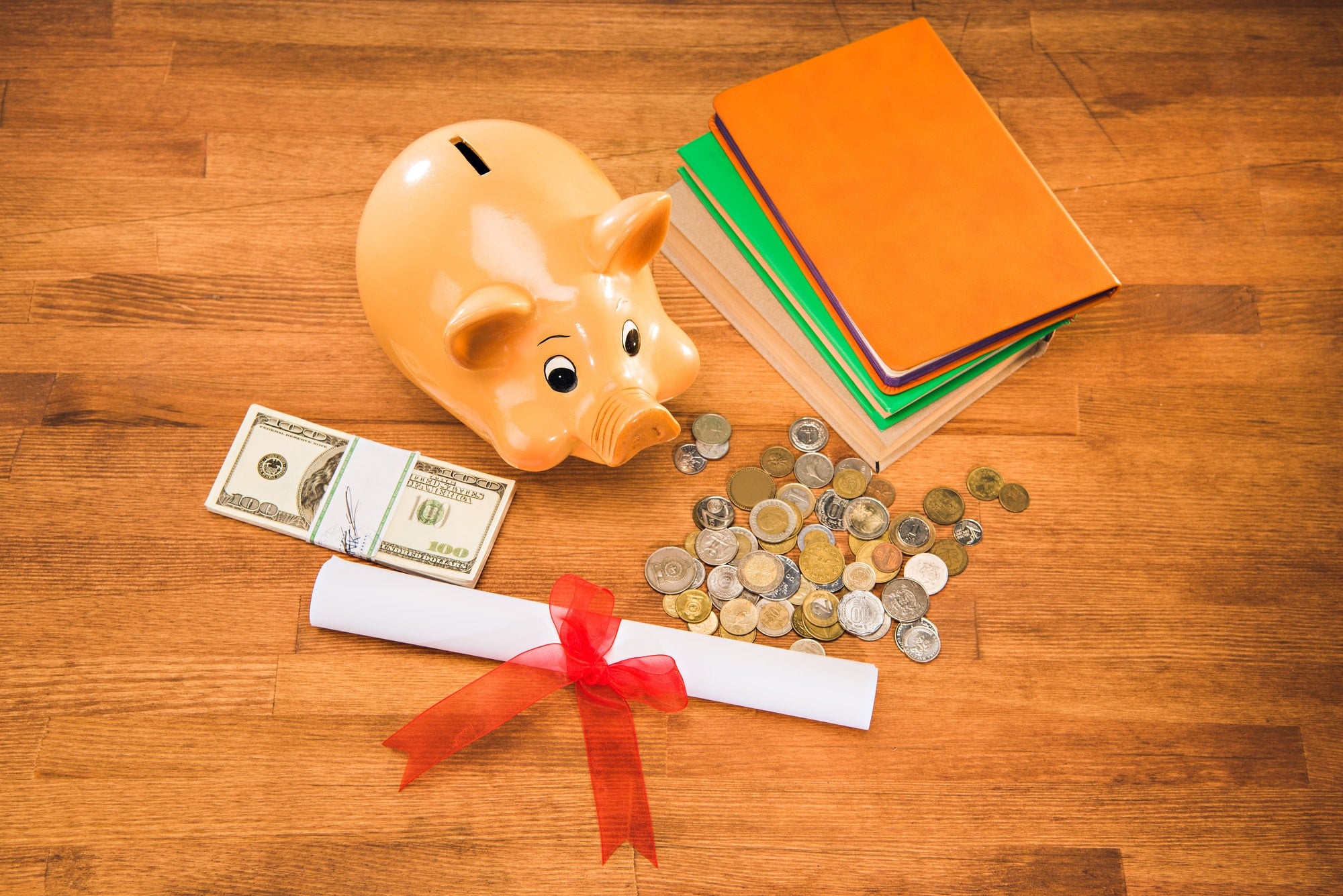 diploma, books and piggy bank with coins and dollars on wooden tabletop, education concept