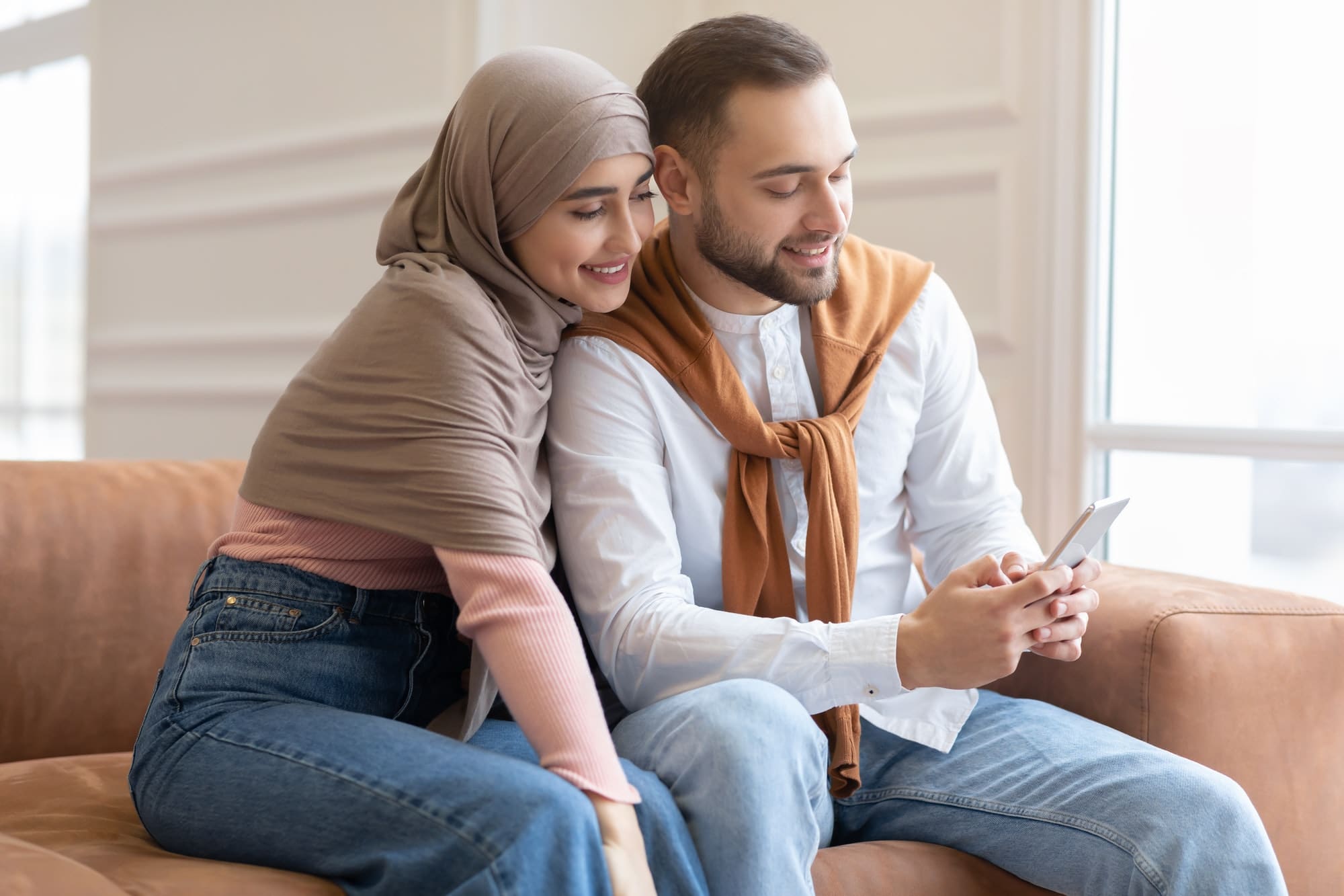 使用智能手机坐在家里的穆斯林夫妇的侧视图